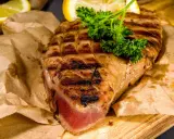 Saftiges Thunfischsteak, perfekt gegrillt, mit Zitronenspalten und Petersilie garniert, auf Packpapier serviert.