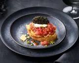 Kaviar Rezepte Vorspeise: Thunfisch-Tatar auf geröstetem Brot, gekrönt mit Kaviar und einem Klecks Crème fraîche. Pistazien und Chips garnieren den Teller.