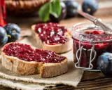 Frisches Brot mit Pflaumenmarmelade ohne Zucker, daneben eine Einmachglas gefüllt mit der leckeren Marmelade und frische Pflaumen.
