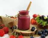 Ein Glas Smoothie, umgeben von frischen Tomaten und Heidelbeeren, die zum Stopfen einladen.