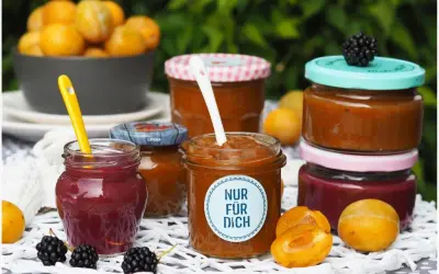 Marmelade ohne Gelierzucker haltbar machen: Mehrere Gläser mit selbstgemachter Marmelade, Früchten und Beeren.