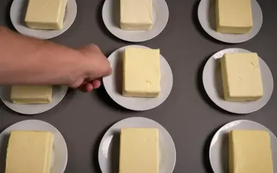 Neun Butterstücke auf Tellern, ein Mann greift nach einem. Die Butter zutaten sind bereit für einen Test.