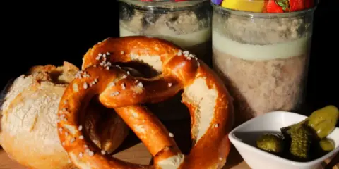 Zwei Gläser mit Fleisch einkochen im Weck-Glas, dazu ein Brezel, Brot und Gewürzgurken.