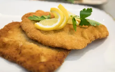 Zwei goldbraune Schnitzel, perfekt in Butter gebraten, garniert mit Zitronenspalten und Petersilie auf einem weißen Teller.