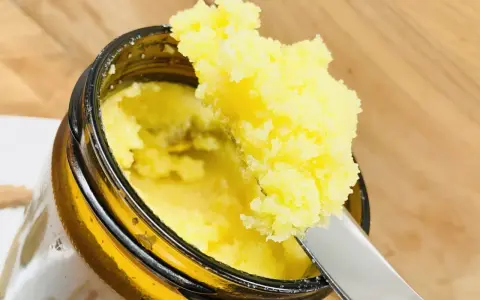 Ein Löffel entnimmt goldgelbes Ghee aus einem Glas. Was ist Ghee? Ein geklärte Butter, ideal zum Kochen und Backen.