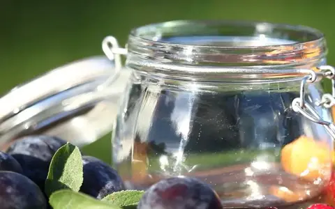 Ein Glas mit frischen Pflaumen und Beeren, bereit für Marmelade. Vorsicht bei der Zubereitung, um Botulismus zu vermeiden.