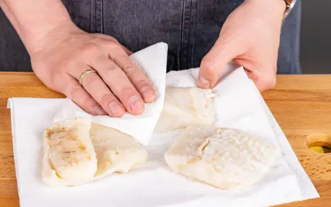 Hände tupfen Steinbeißer Fischfilets auf Küchenpapier trocken, bereit für die Zubereitung.