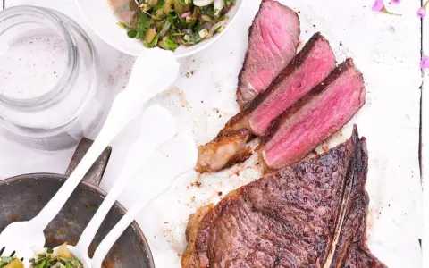 Perfekt gegrillter T-Bone-Steak, saftig rosa im Inneren, mit Beilagensalat und grobem Salz. Die t-bone steak zubereitung ist ein Genuss.
