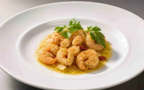 Saftige, gebackene Garnelen mit Knoblauch und Petersilie auf einem weißen Teller.