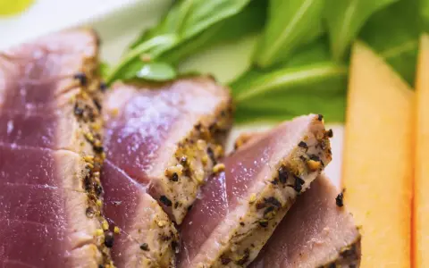 Saftiges Thunfischfilet, perfekt angebraten, mit Gewürzkruste, serviert mit frischem Grün und Honigmelone.