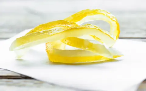 Gelbe Zitronenschalen-Streifen, die an das Selbermachen von Apfelpektin erinnern, liegen auf weißem Papier.