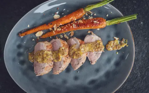 Zartes schweinefilet grillen, serviert mit karamellisierten Karotten und grobem Senf. Geröstete Mandelsplitter runden das Gericht ab.