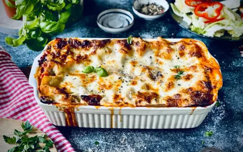 Herzhafte vegetarische Lasagne mit geschmolzenem Käse und frischem Basilikum, serviert in einer weißen Auflaufform.