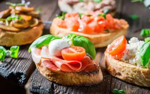 Verschiedene herzhafte Snacks auf geröstetem Brot: Bruschetta mit Tomaten, Pilzen, Schinken und Mozzarella.