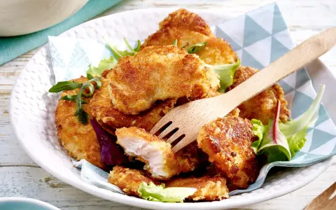 Knusprige Hähnchen-Nuggets, perfekt im Butterschmalz gebraten, auf einem Bett aus Salat. Ein Holzgabel liegt bereit.
