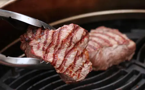 Zangen halten ein saftiges Stück Roastbeef, das auf einem Grill zubereitet wird.