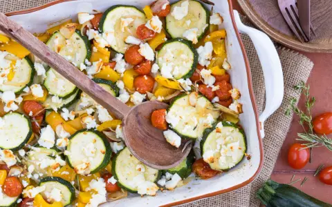Gebackener Feta mit Zucchini, Kirschtomaten und gelber Paprika in einer Auflaufform, bereit zum Servieren.