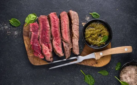 Saftiges, aufgeschnittenes Fleisch zum Grillen, serviert mit Kräutersauce und Gewürzen.