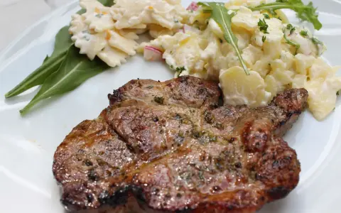 Saftiges Nackensteak grillen mit Kartoffel- und Nudelsalat auf einem weißen Teller.