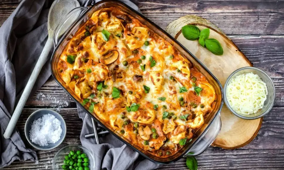 Herzhafter Tortellini Auflauf mit Erbsen und Pilzen, überbacken mit Käse und garniert mit frischem Basilikum.