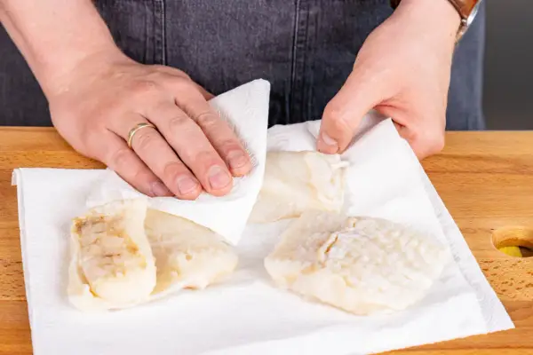 Hände tupfen Steinbeißer Fischfilets auf Küchenpapier trocken, bereit für die Zubereitung.