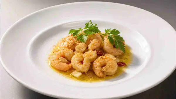 Saftige, gebackene Garnelen mit Knoblauch und Petersilie auf einem weißen Teller.