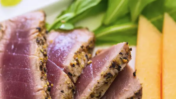 Saftiges Thunfischfilet, perfekt angebraten, mit Gewürzkruste, serviert mit frischem Grün und Honigmelone.