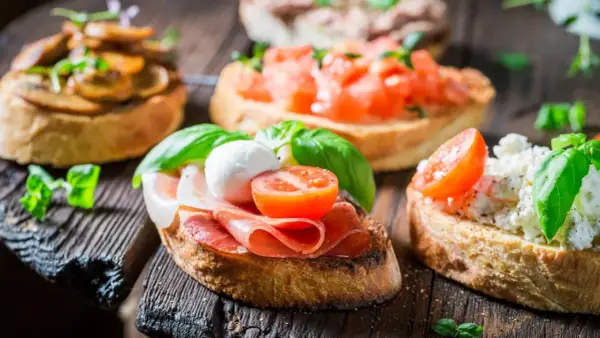 Verschiedene herzhafte Snacks auf geröstetem Brot: Bruschetta mit Tomaten, Pilzen, Schinken und Mozzarella.