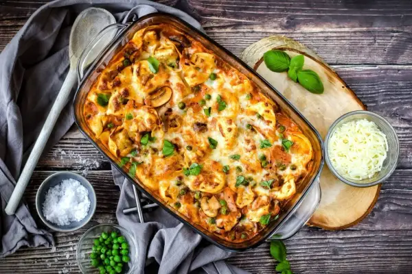 Herzhafter Tortellini Auflauf mit Erbsen und Pilzen, überbacken mit Käse und garniert mit frischem Basilikum.