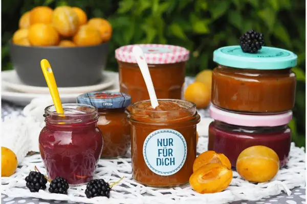 Marmelade ohne Gelierzucker haltbar machen: Mehrere Gläser mit selbstgemachter Marmelade, Früchten und Beeren.