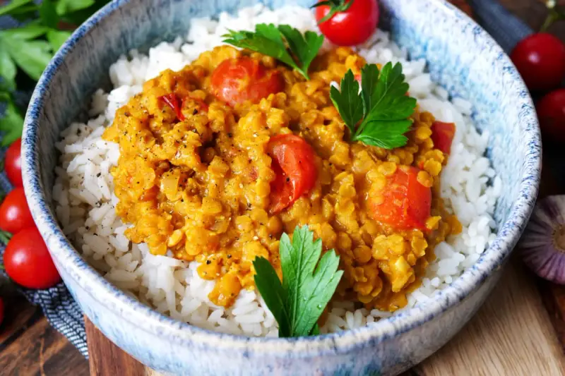 Herzhaftes rote Linsen Curry mit Reis, garniert mit frischer Petersilie und Kirschtomaten. Ein Genuss für die Sinne!